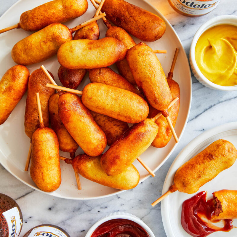 Plates of home-made mini corn dogs and bowls of ketchup and mustard.