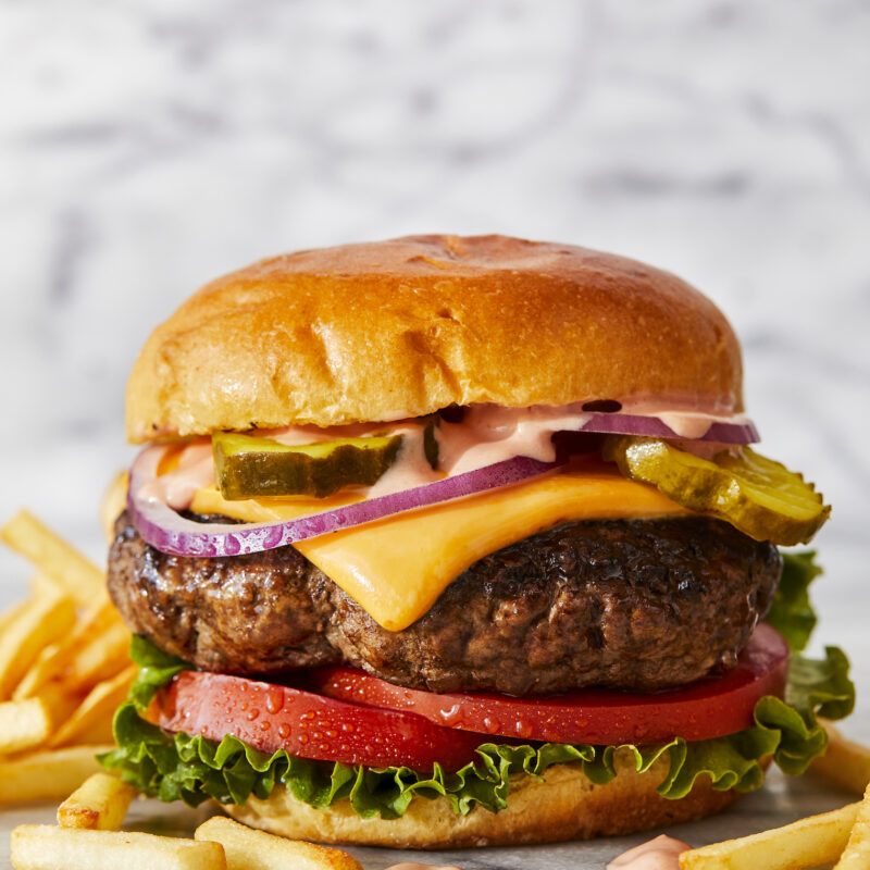 A juicy hamburger on a brioche bun, garnished with lettuce, tomato slices, dill pickles, red onion slices and melted cheese.