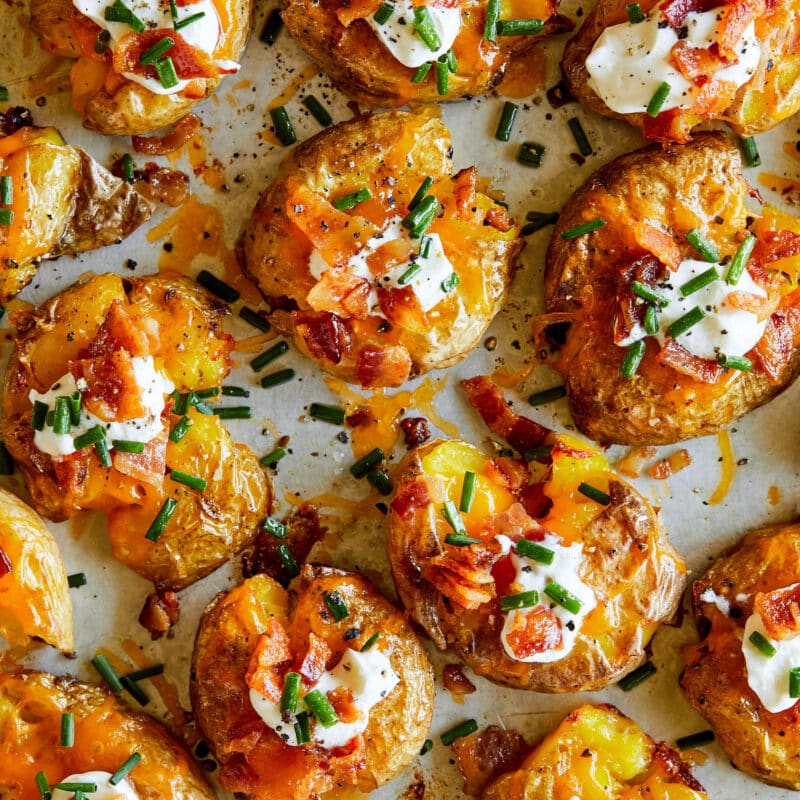 Super crispy smashed potatoes topped with sour cream, bacon and chives, resting in an oven pan.