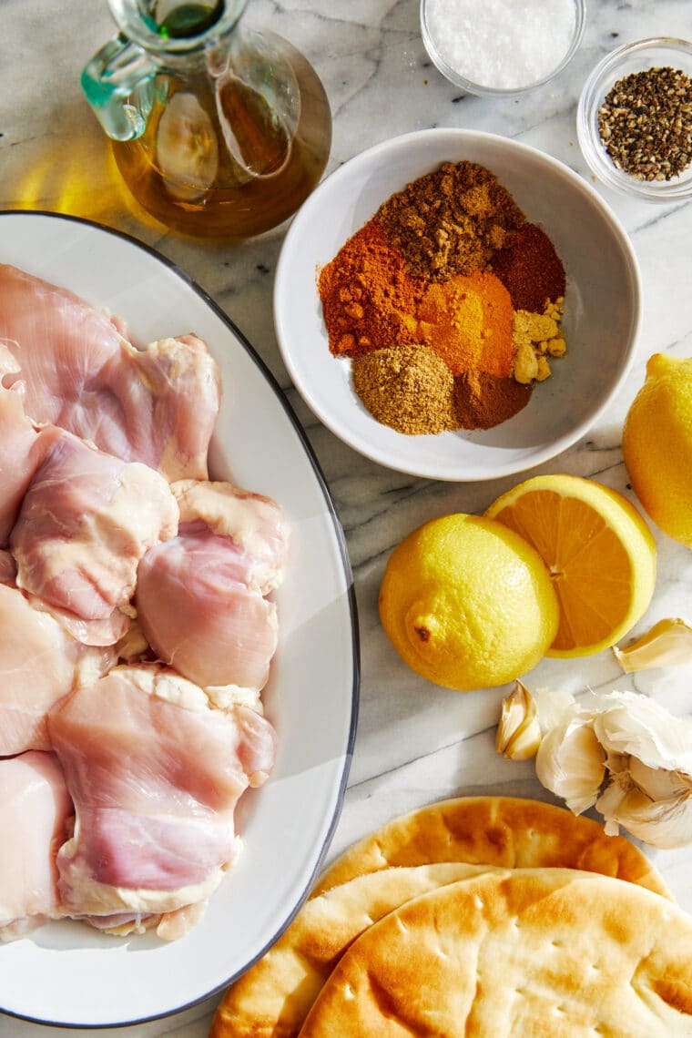 Raw, boneless, skinless chicken thighs, olive oil, fresh lemons and garlic, and spices for the shawarma marinade. 