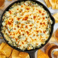 A cheesy, spinach and artichoke dip served in a cast iron skillet, resting on a marble counter top.