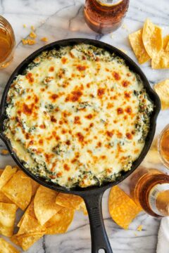 A cheesy, spinach and artichoke dip served in a cast iron skillet, resting on a marble counter top.