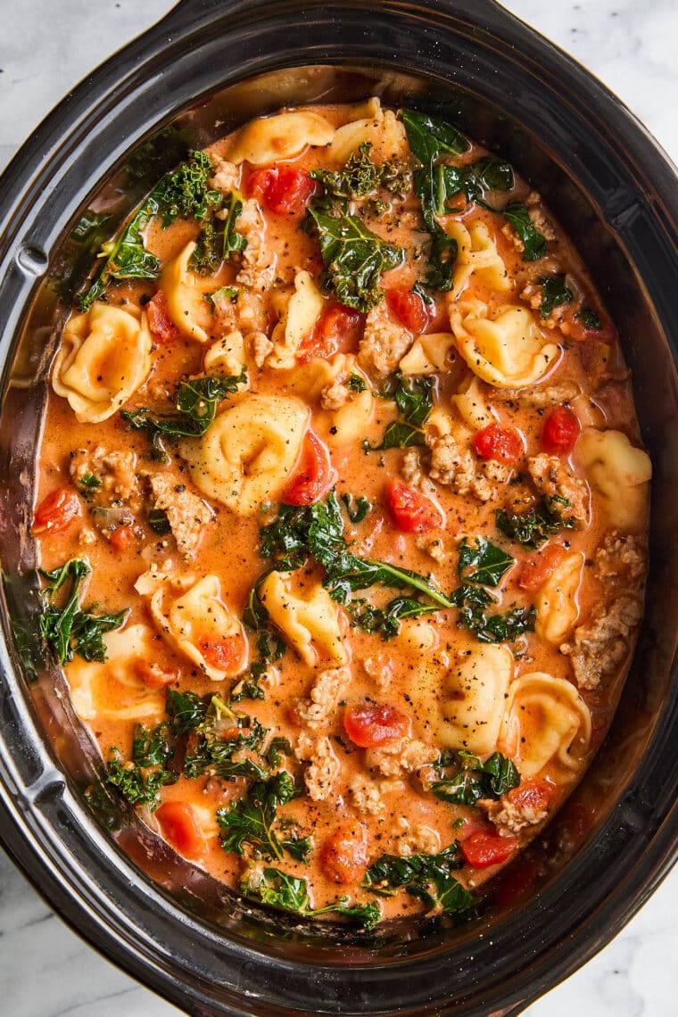 Slow Cooker Tortellini Soup - With crumbled sausage, tomatoes, pillowy cheese tortellini + leafy greens in a velvety, creamy broth. SO GOOD!